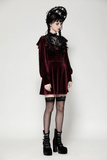 Model in burgundy velvet dress with black lace trim and ruffles, wearing puffy sleeves and striking platform heels.